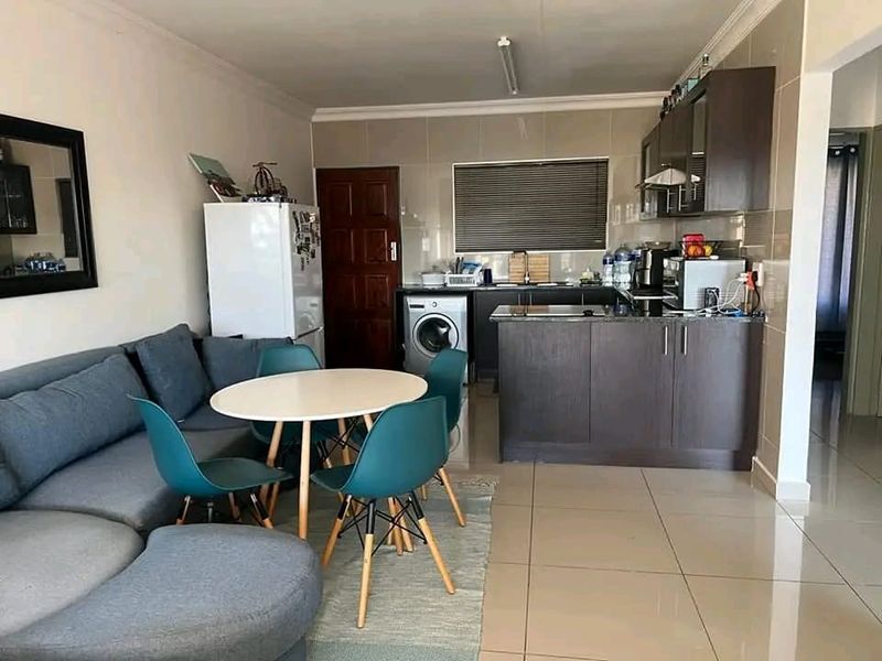 Open-plan living area featuring a compact kitchen with dark cabinetry, granite countertops, and tiled flooring, seamlessly integrated with the dining and lounge space.