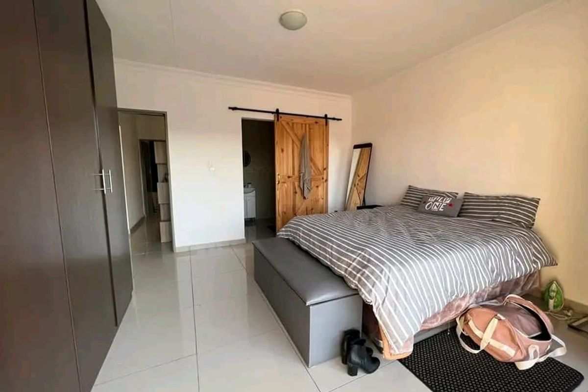 A well-maintained bedroom featuring modern tiled flooring, built-in cupboards, and a rustic sliding barn door leading to an en-suite bathroom.