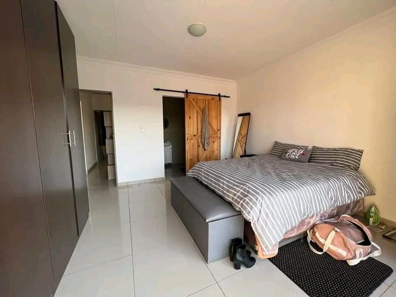A well-maintained bedroom featuring modern tiled flooring, built-in cupboards, and a rustic sliding barn door leading to an en-suite bathroom.