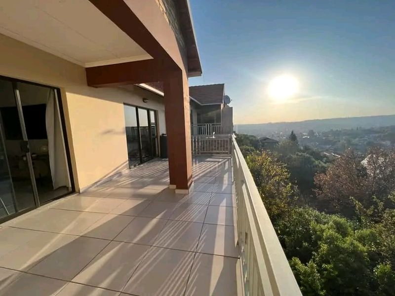 A spacious covered balcony featuring tiled flooring, secure railings, and sliding glass door access, offering expansive elevated views.