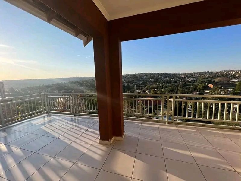 A spacious covered balcony featuring tiled flooring and a metal balustrade, offering expansive elevated views of the surrounding neighborhood.