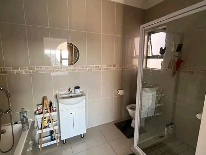 A functional bathroom featuring a separate shower enclosure, bathtub, vanity cabinet with basin, and neutral wall and floor tiling.