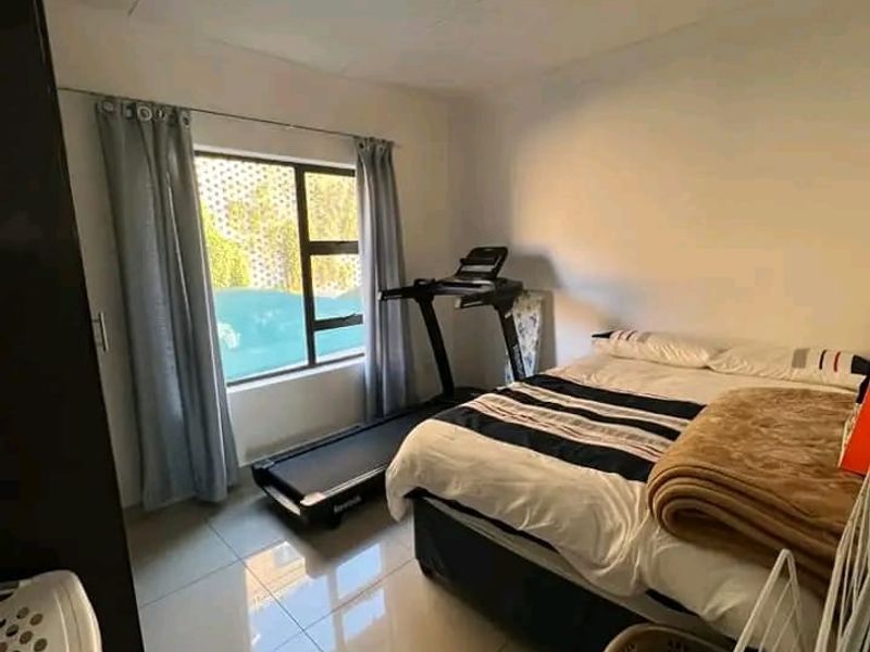A functional bedroom featuring tiled flooring, a built-in cupboard, and an aluminium-framed window providing natural light.