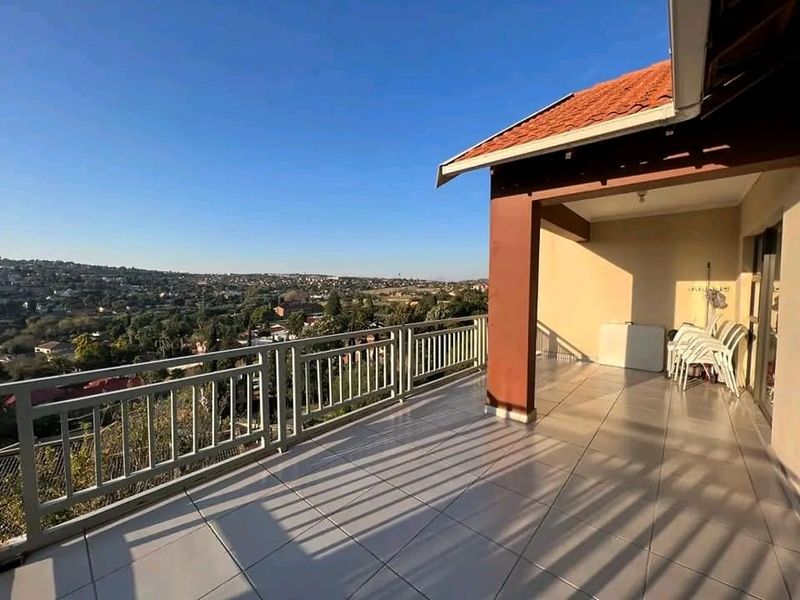 A spacious covered balcony featuring tiled flooring and a metal balustrade, offering expansive elevated views of the surrounding neighborhood.