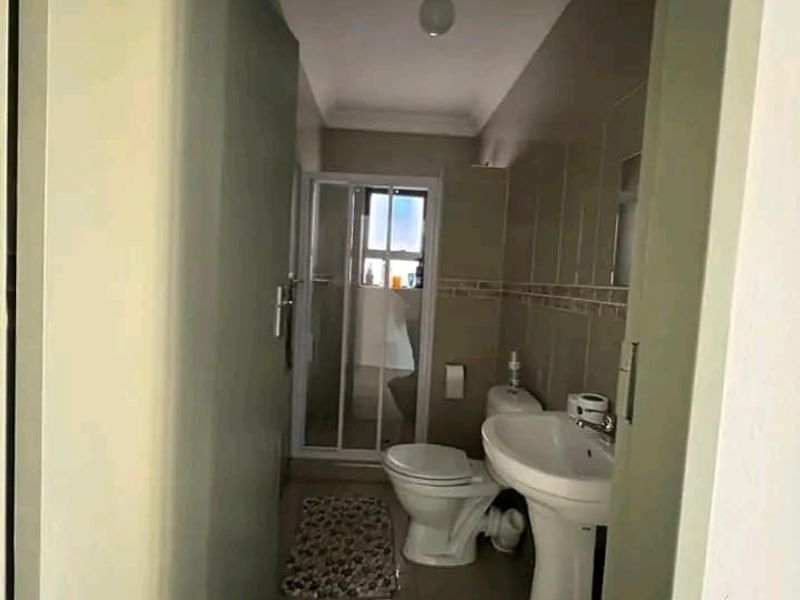 A compact bathroom featuring a pedestal sink, toilet, and a separate shower enclosure with tiled walls and flooring.