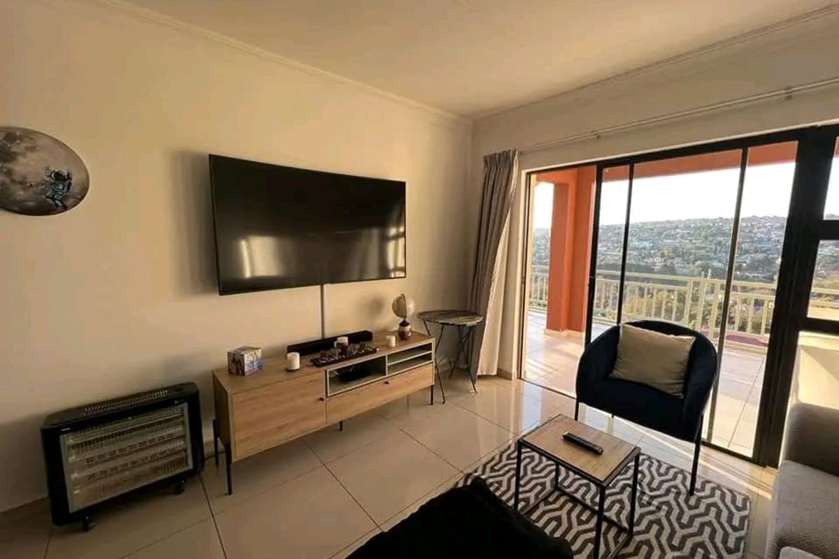 A bright living room featuring tiled flooring and large sliding glass doors that open onto a balcony with scenic views.