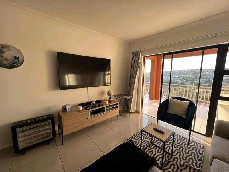 A bright living room featuring tiled flooring and large sliding glass doors that open onto a balcony with scenic views.