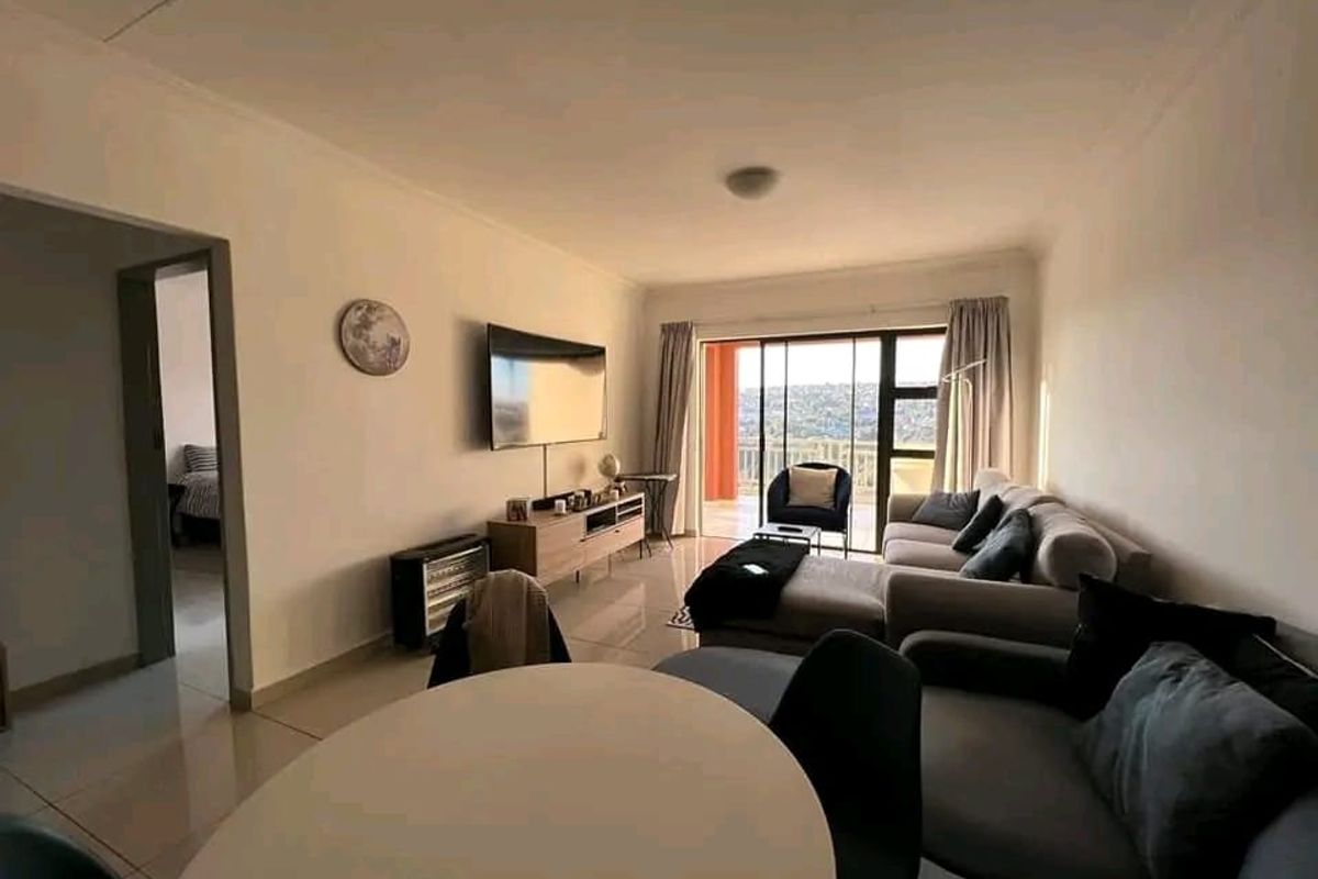 A bright and spacious living room featuring tiled flooring and a large sliding glass door that provides access to an outdoor balcony area.