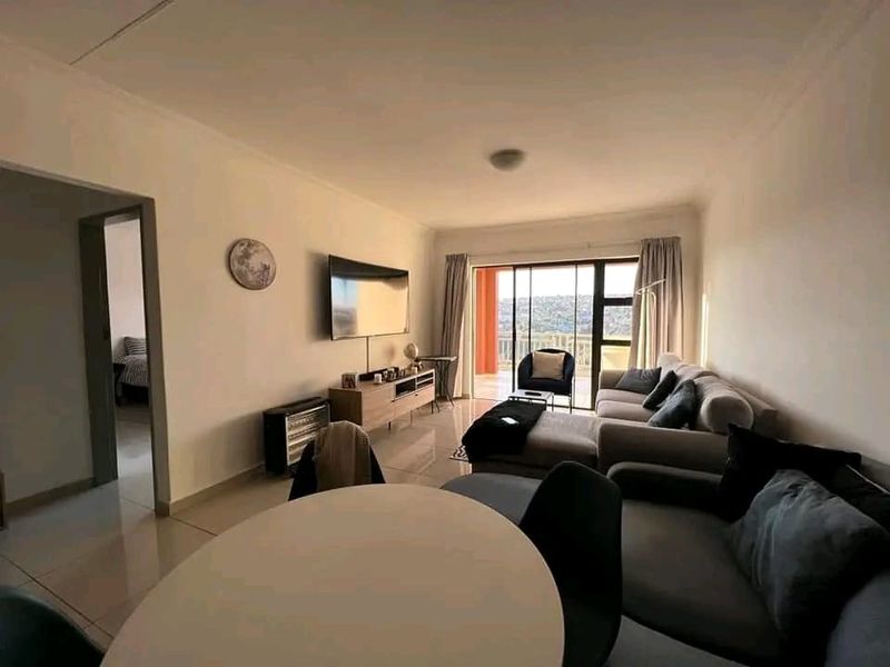 A bright and spacious living room featuring tiled flooring and a large sliding glass door that provides access to an outdoor balcony area.