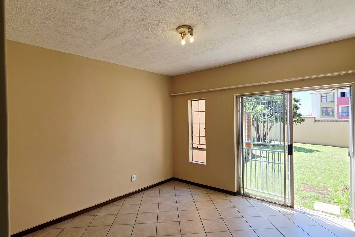 An empty living room featuring ceramic floor tiles, a textured ceiling, and a sliding glass door providing access to the garden.