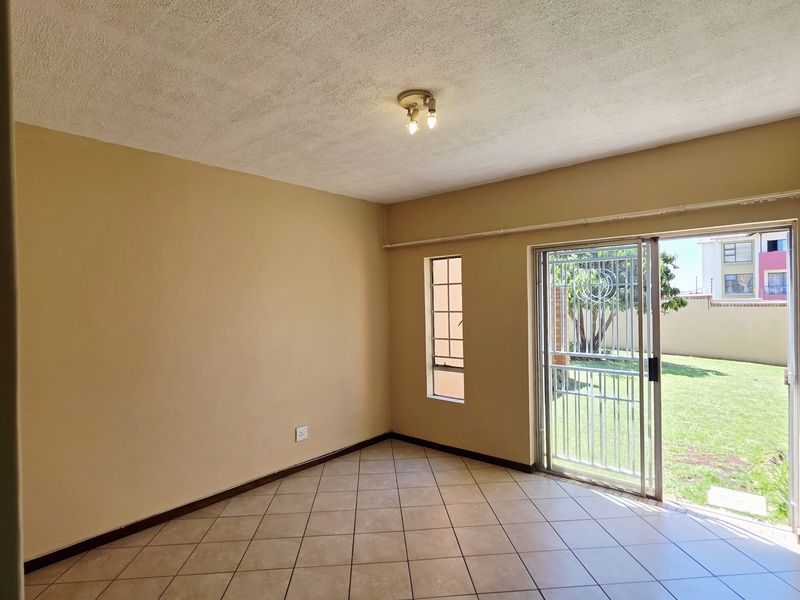 An empty living room featuring ceramic floor tiles, a textured ceiling, and a sliding glass door providing access to the garden.