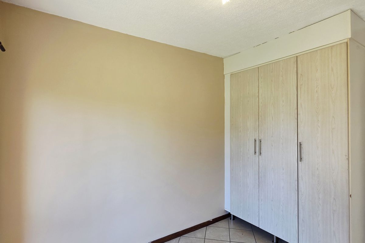 A clean, empty bedroom featuring neutral wall tones, tiled flooring, and a functional built-in wardrobe with light wood-grain finish.