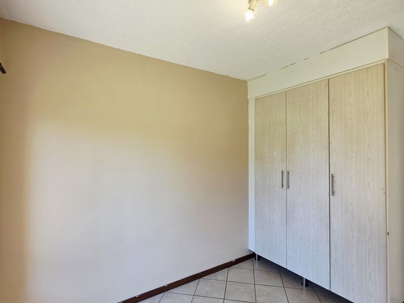 A clean, empty bedroom featuring neutral wall tones, tiled flooring, and a functional built-in wardrobe with light wood-grain finish.