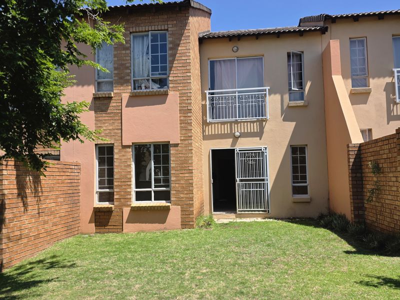Rear view of a two-story apartment featuring a private garden, brick facade, balcony with metal railing, and secure sliding door access.
