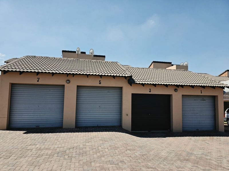 A row of four numbered garage units featuring roller shutter doors and a paved driveway area.