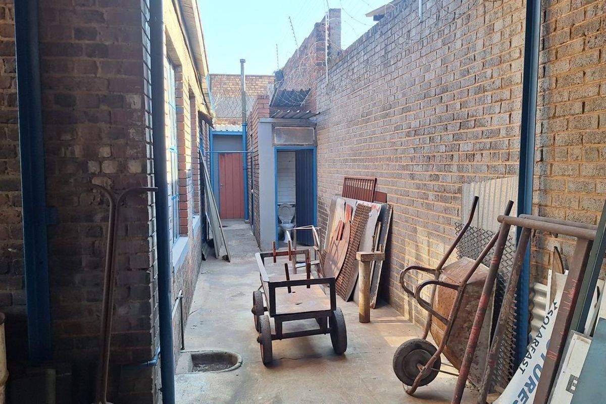 A narrow exterior side passage featuring exposed brick walls, concrete flooring, and access to a small outdoor utility area with a toilet.