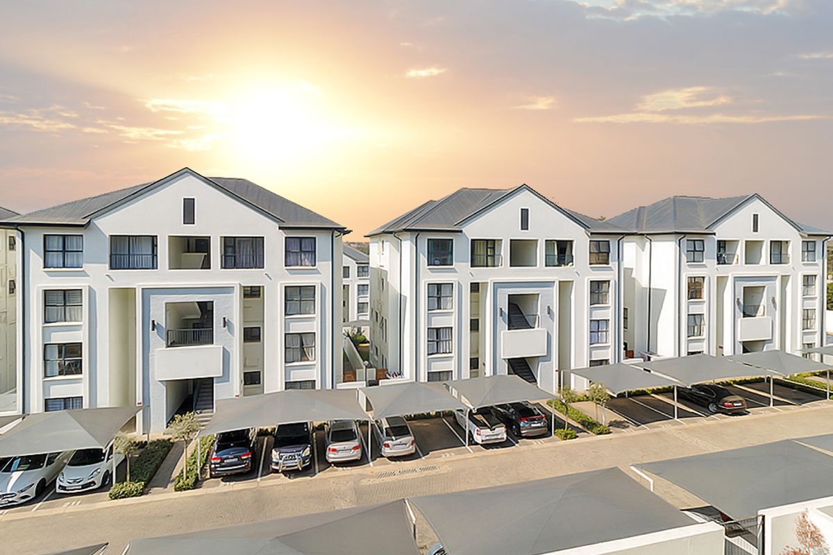 Aerial view of a modern apartment complex featuring multi-story residential buildings with covered parking bays and landscaped surroundings at sunset.