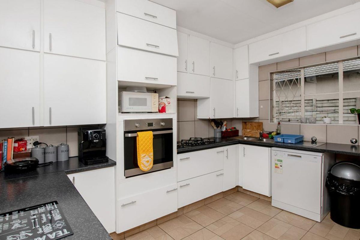 Functional kitchen featuring white cabinetry, dark laminate countertops, built-in oven, gas hob, and tiled flooring with a window overlooking the exterior.