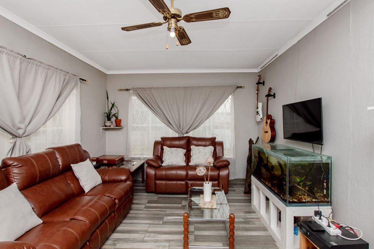 A comfortable living room featuring wood-look tile flooring, a ceiling fan, and large windows with curtain treatments.