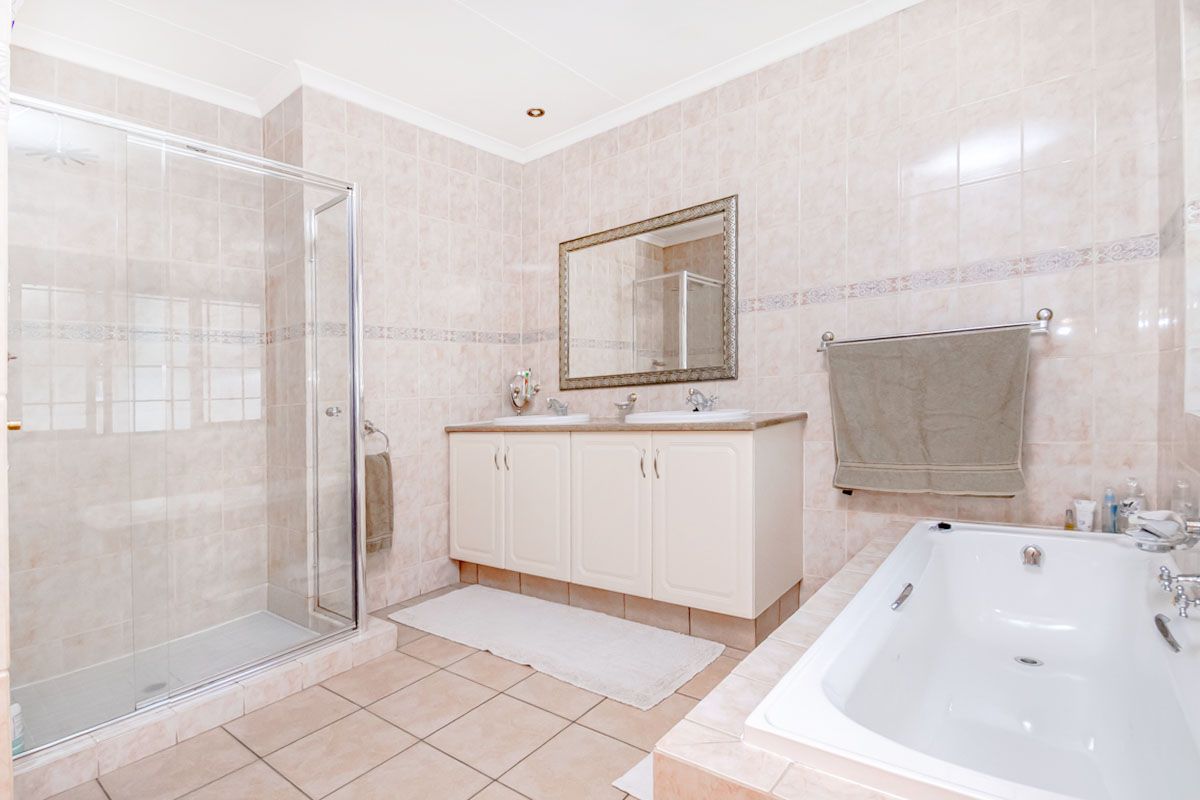 A spacious bathroom featuring a double vanity, a glass-enclosed shower, and a built-in bathtub with neutral wall and floor tiling.
