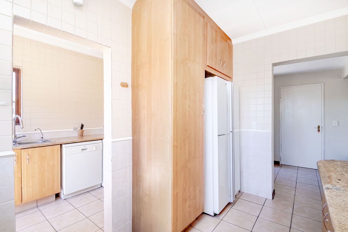 A functional kitchen area featuring light wood cabinetry, tiled walls, and a dedicated scullery space with a sink and dishwasher connection.