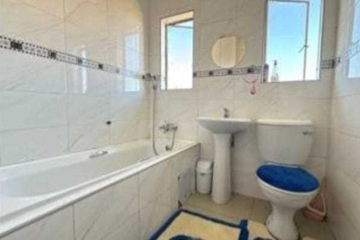 A functional bathroom featuring a pedestal basin, bathtub, and toilet with tiled walls and natural light from two windows.