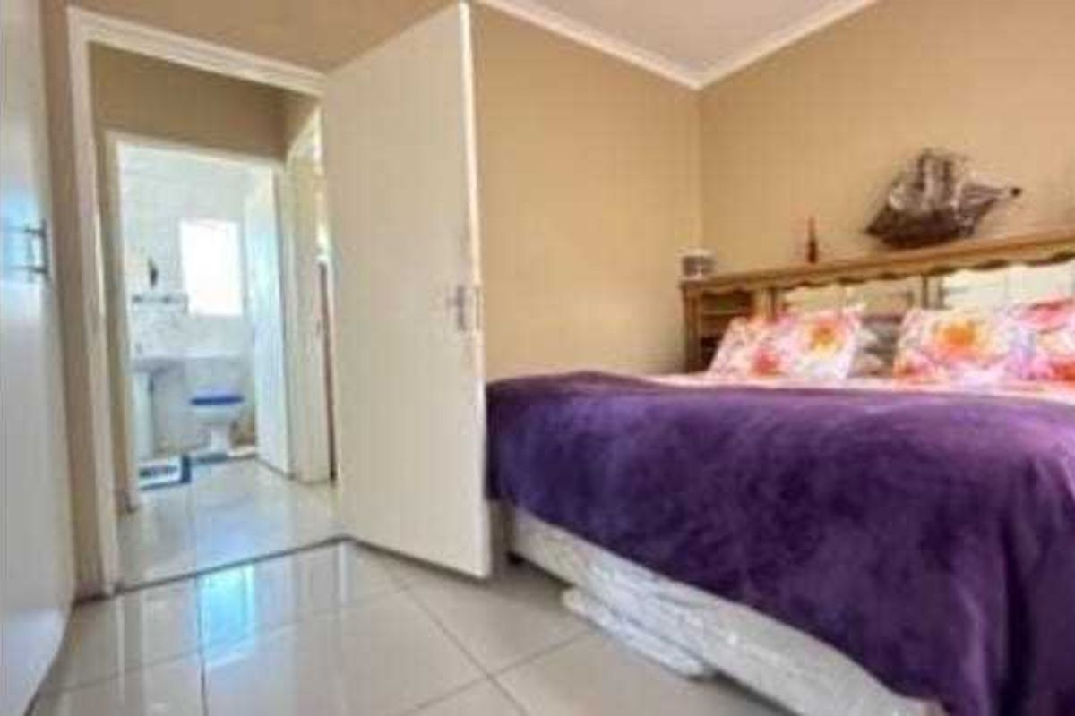 A bedroom featuring tiled flooring and built-in cupboards, with an adjoining en-suite bathroom visible through the doorway.