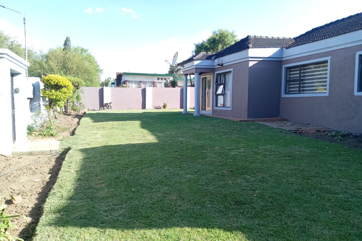 A spacious rear garden featuring a well-maintained lawn, perimeter boundary walls, and a covered patio area attached to the main house structure.