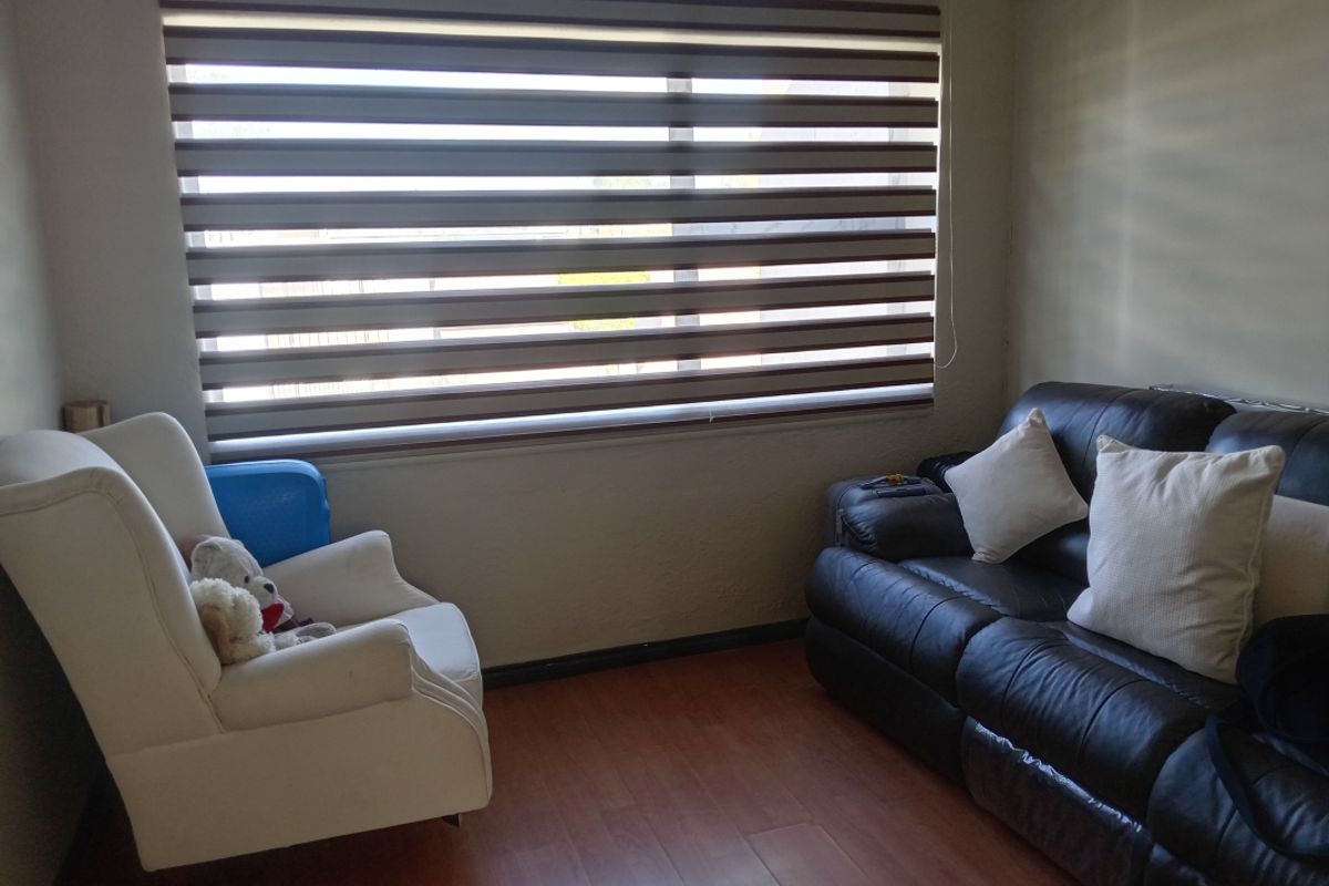 A cozy living room featuring wood-look flooring and a large window fitted with modern zebra-style roller blinds.