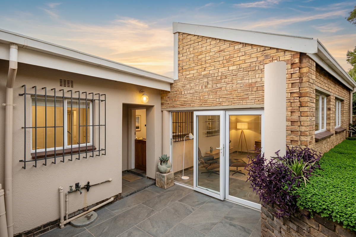 A well-maintained rear exterior view featuring a paved patio, brick facade, and modern glass sliding doors leading into the home.