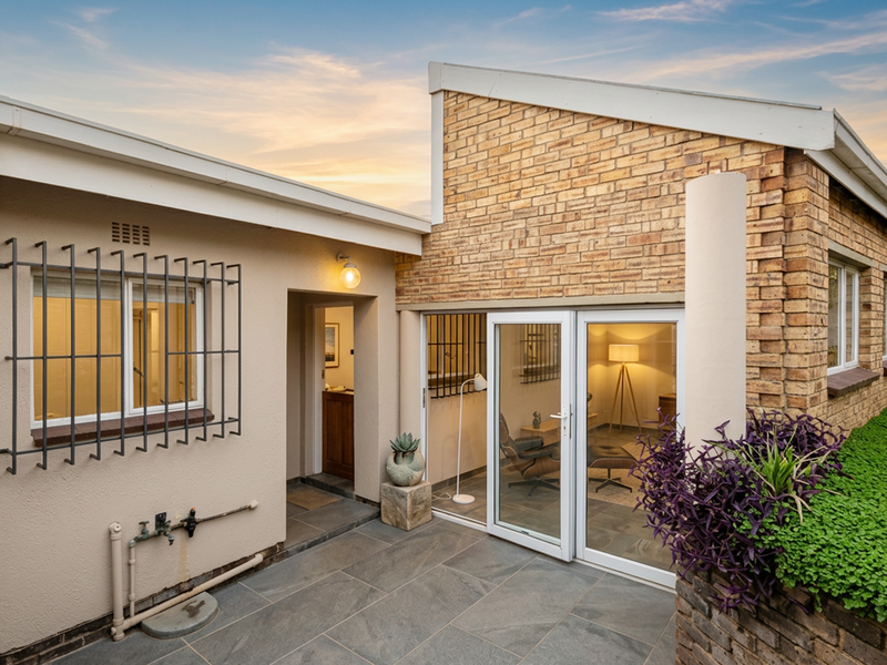 A well-maintained rear exterior view featuring a paved patio, brick facade, and modern glass sliding doors leading into the home.