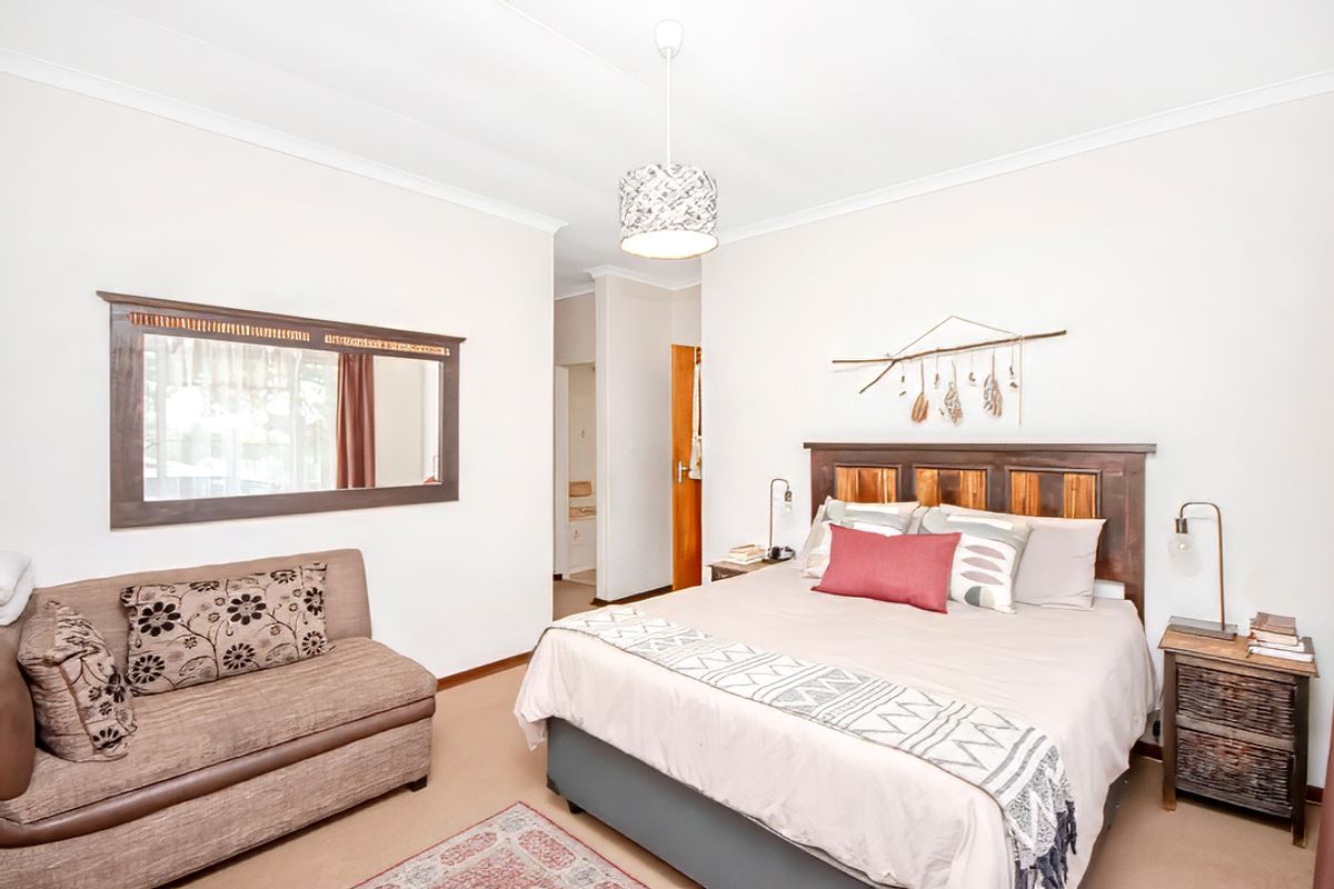 A well-lit bedroom featuring neutral walls, carpeted flooring, and a built-in doorway leading to an adjacent space.