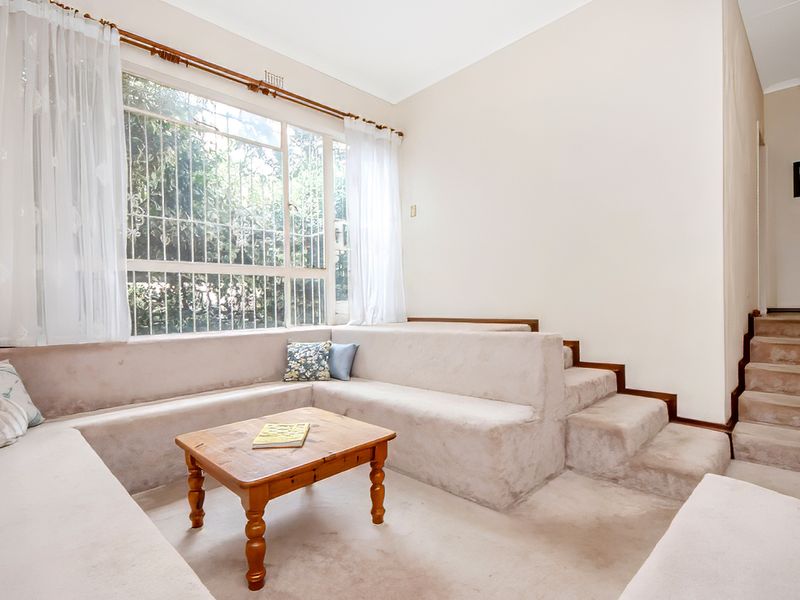 Sunlit living area featuring a unique built-in sunken lounge seating arrangement, large windows with security bars, and carpeted flooring.