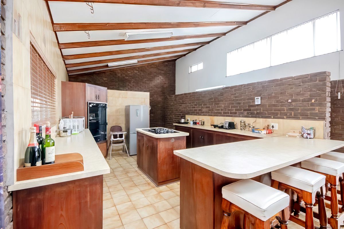 Spacious kitchen featuring wooden cabinetry, a central island with a built-in hob, and exposed timber ceiling beams.