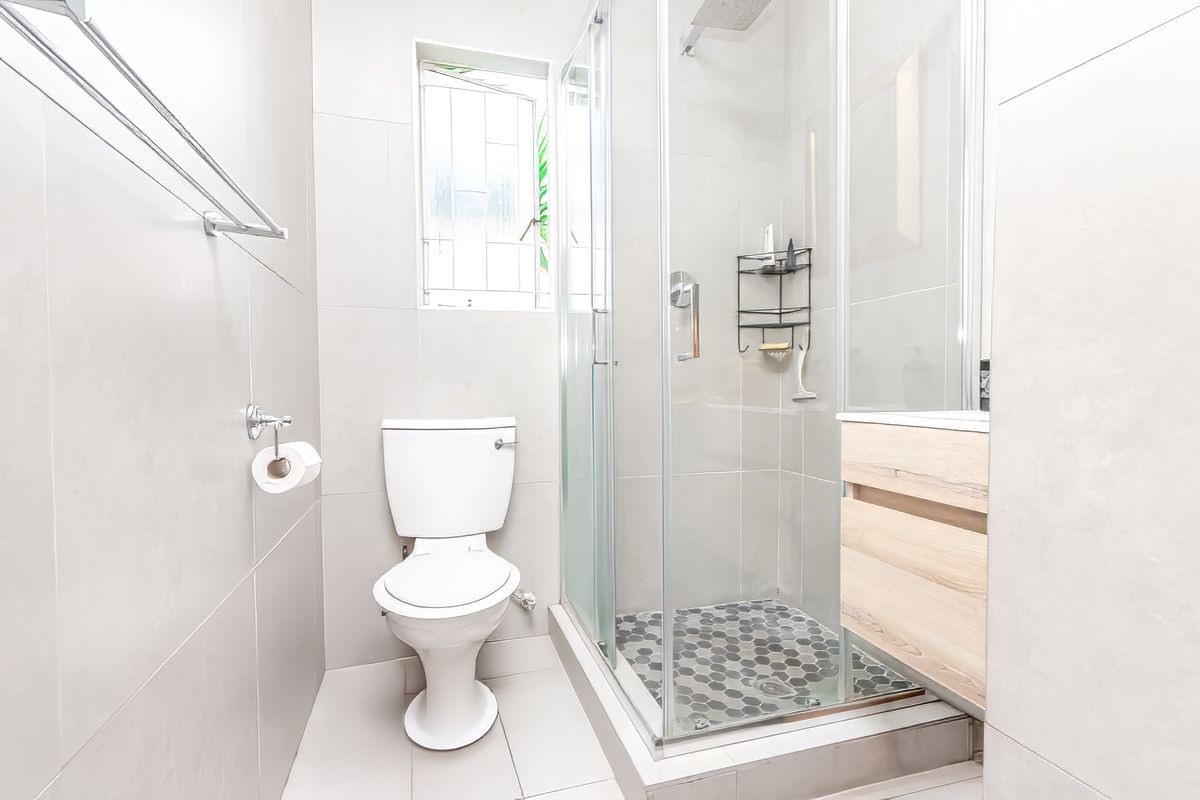 Modern bathroom featuring a glass-enclosed shower with mosaic tile flooring, a wall-mounted vanity, and a white toilet.