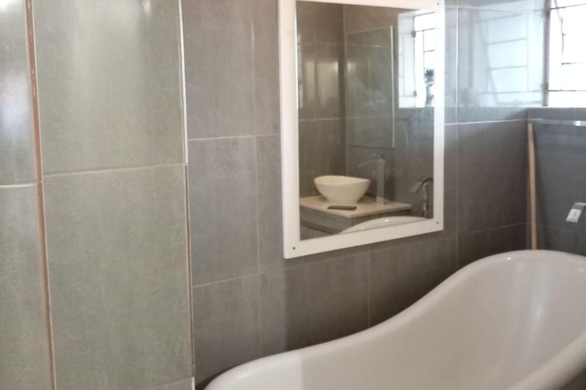 A modern bathroom featuring a white freestanding bathtub, grey wall tiling, and a wall-mounted mirror.