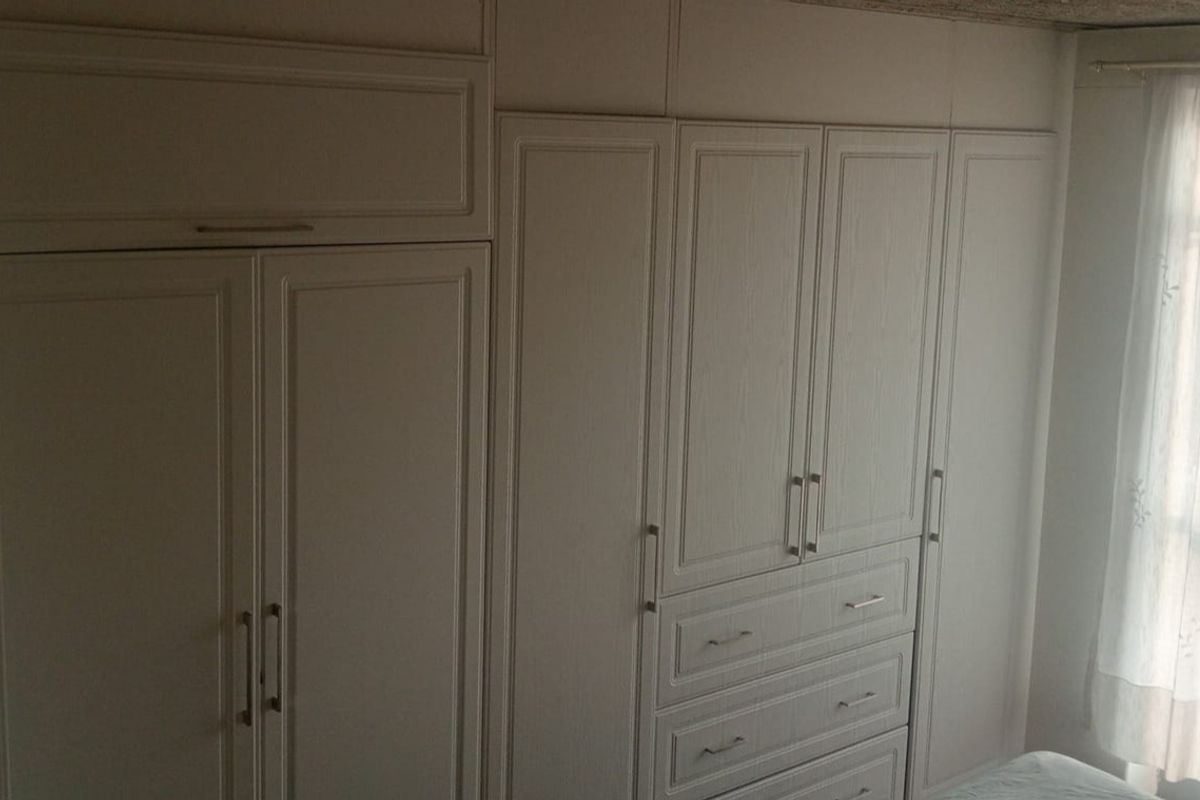 A bedroom featuring extensive white built-in cabinetry with integrated storage drawers and overhead cupboards.