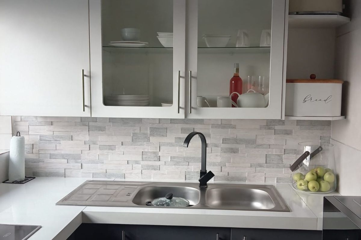 A modern kitchen featuring dark grey lower cabinets, white upper glass-fronted cupboards, a double stainless steel sink with a black mixer tap, and a textured splashback.