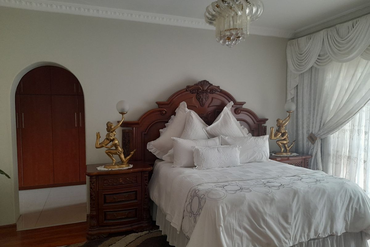 A well-maintained bedroom featuring classic crown molding, a built-in arched wooden wardrobe, and elegant drapery.