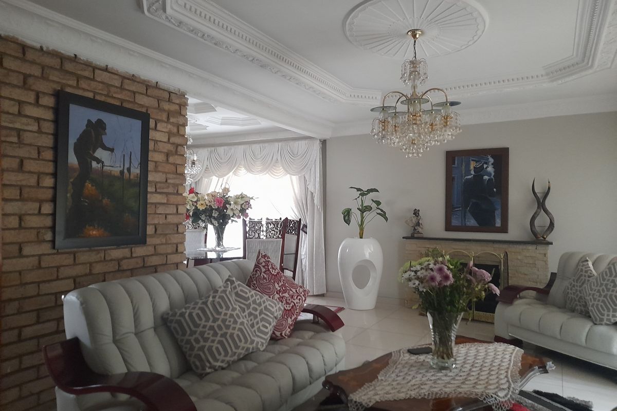 Spacious living area featuring a decorative brick accent wall, ornate ceiling cornices, a central chandelier, and a built-in fireplace.