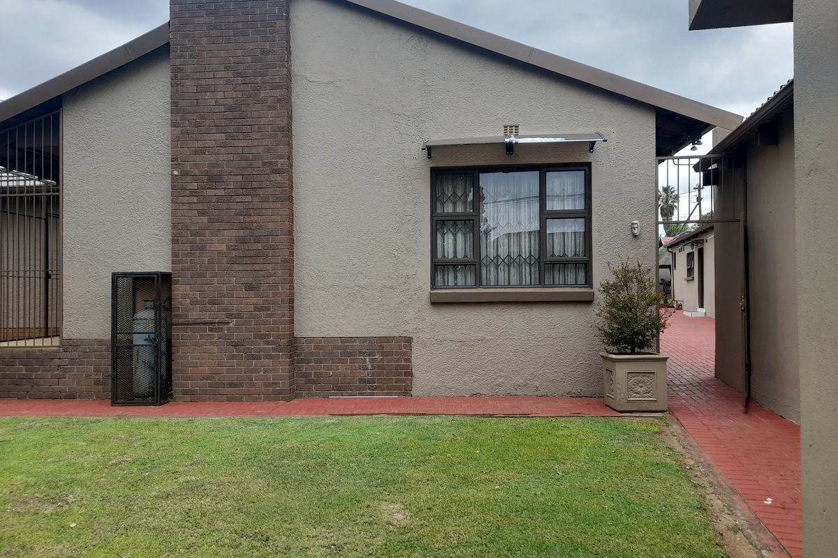 Exterior view of the property featuring a brick chimney, paved pathways, and a well-maintained lawn area.
