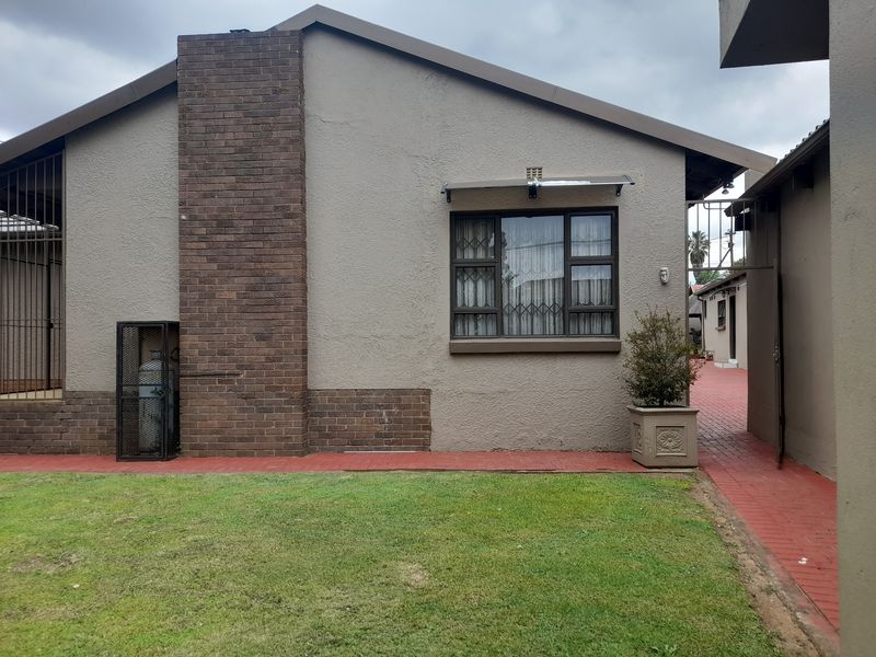Exterior view of the property featuring a brick chimney, paved pathways, and a well-maintained lawn area.