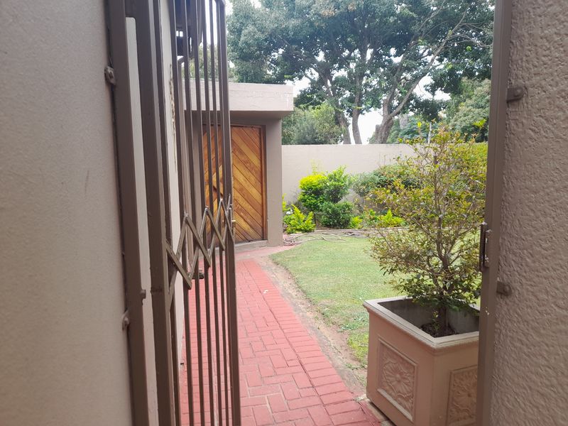 A view through a metal security gate leading to a paved walkway, small garden area, and wooden door entrance.