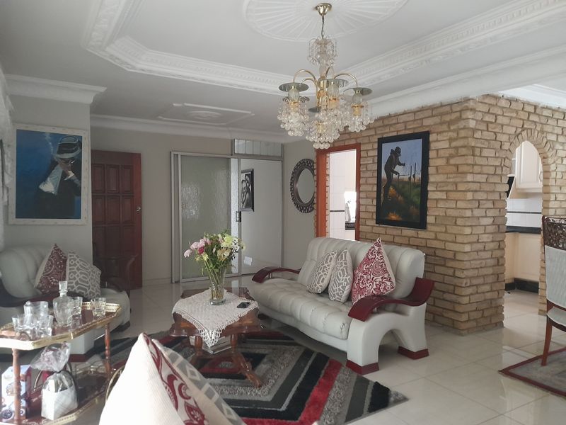 Open plan living area featuring a decorative ceiling rose, crystal chandelier, and a rustic brick partition wall leading to the kitchen.