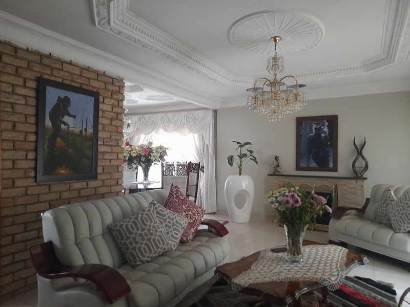 Spacious living area featuring a decorative brick accent wall, ornate ceiling cornices, a central chandelier, and a built-in fireplace.