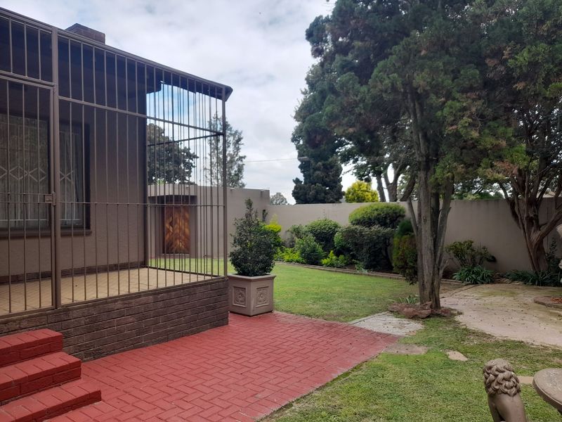 A private rear garden featuring a paved patio area, established trees, and a secure enclosed porch attached to the main dwelling.
