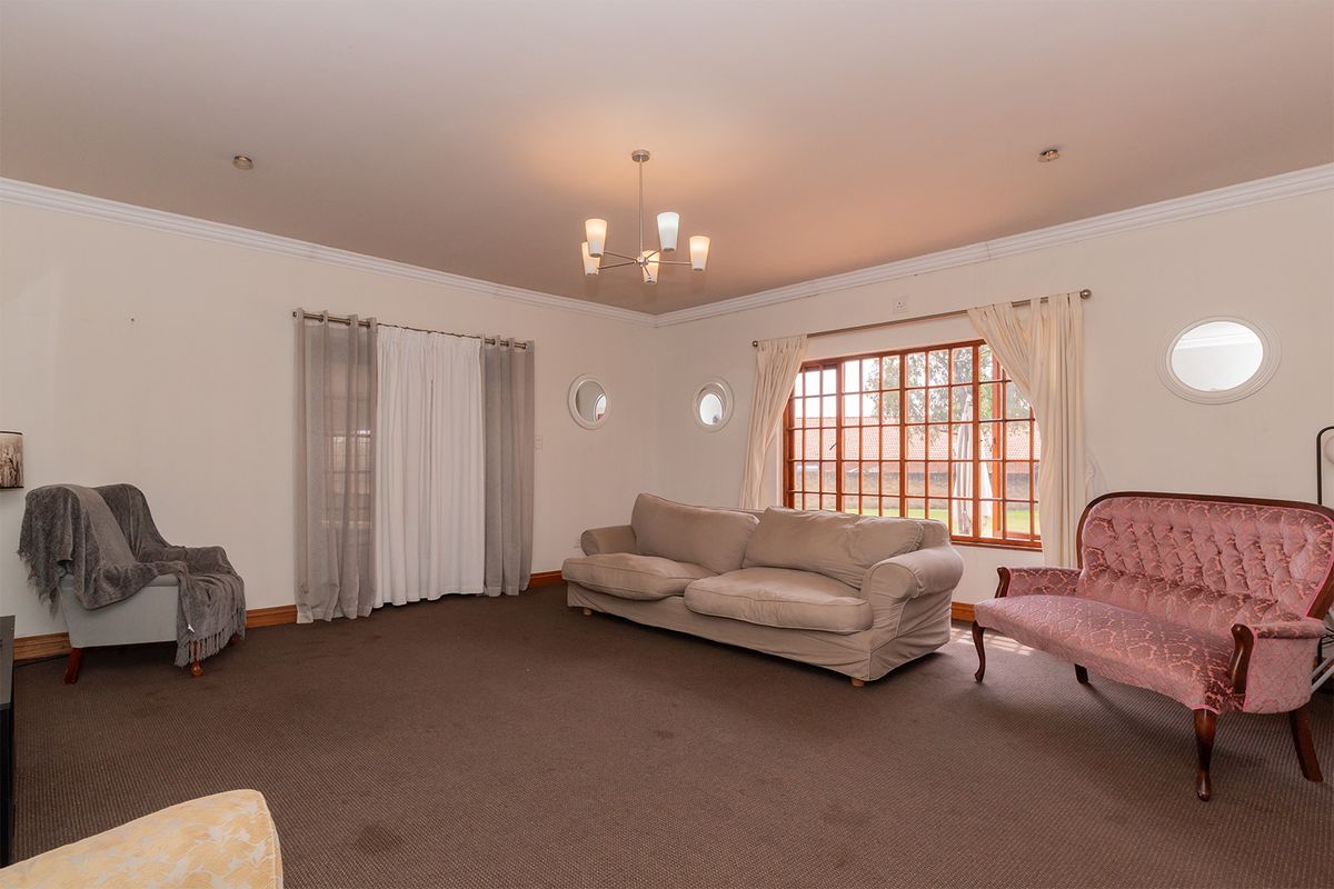 Spacious living room featuring neutral walls, crown molding, carpeted flooring, and large windows with wooden frames allowing for natural light.