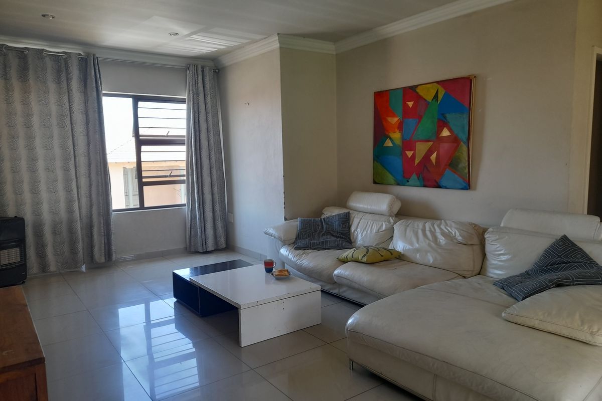 A spacious living room featuring large format floor tiles, crown molding, and a window with security bars, offering a bright and functional living space.