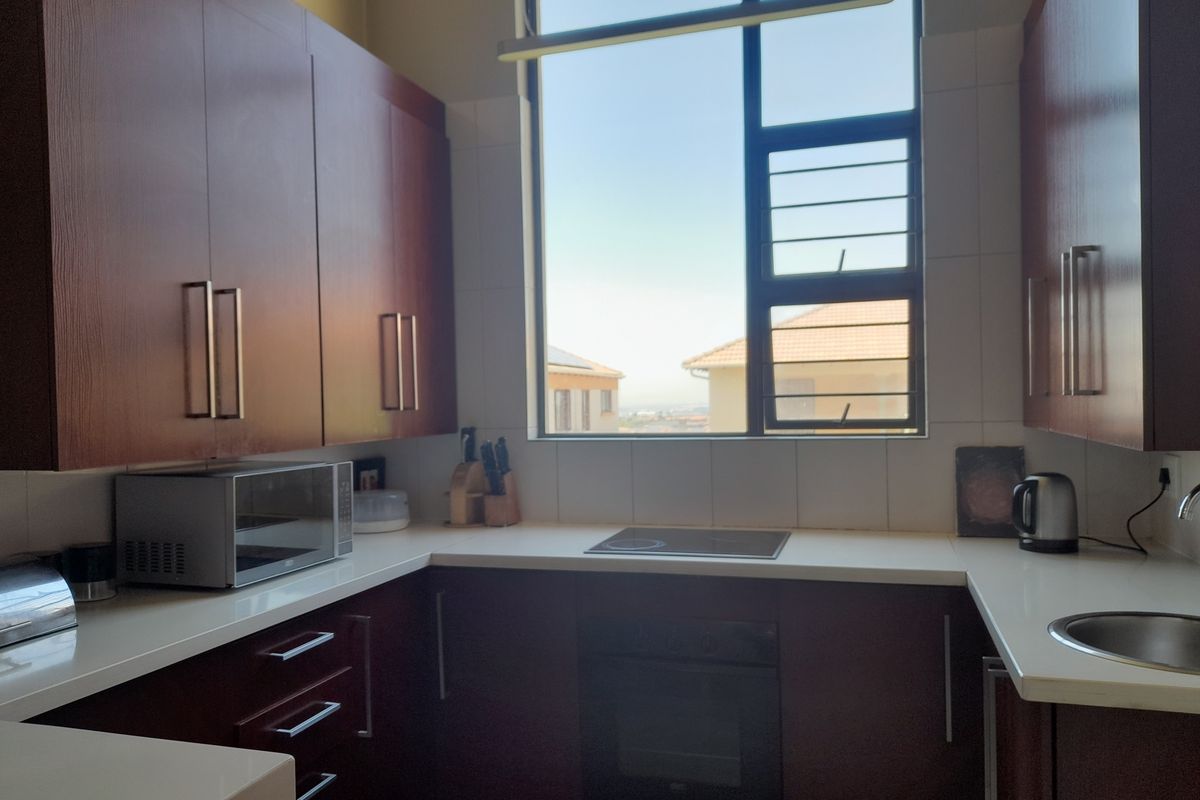 A functional kitchen featuring dark wood cabinetry, white countertops, a built-in oven, and a glass cooktop, illuminated by a large window.