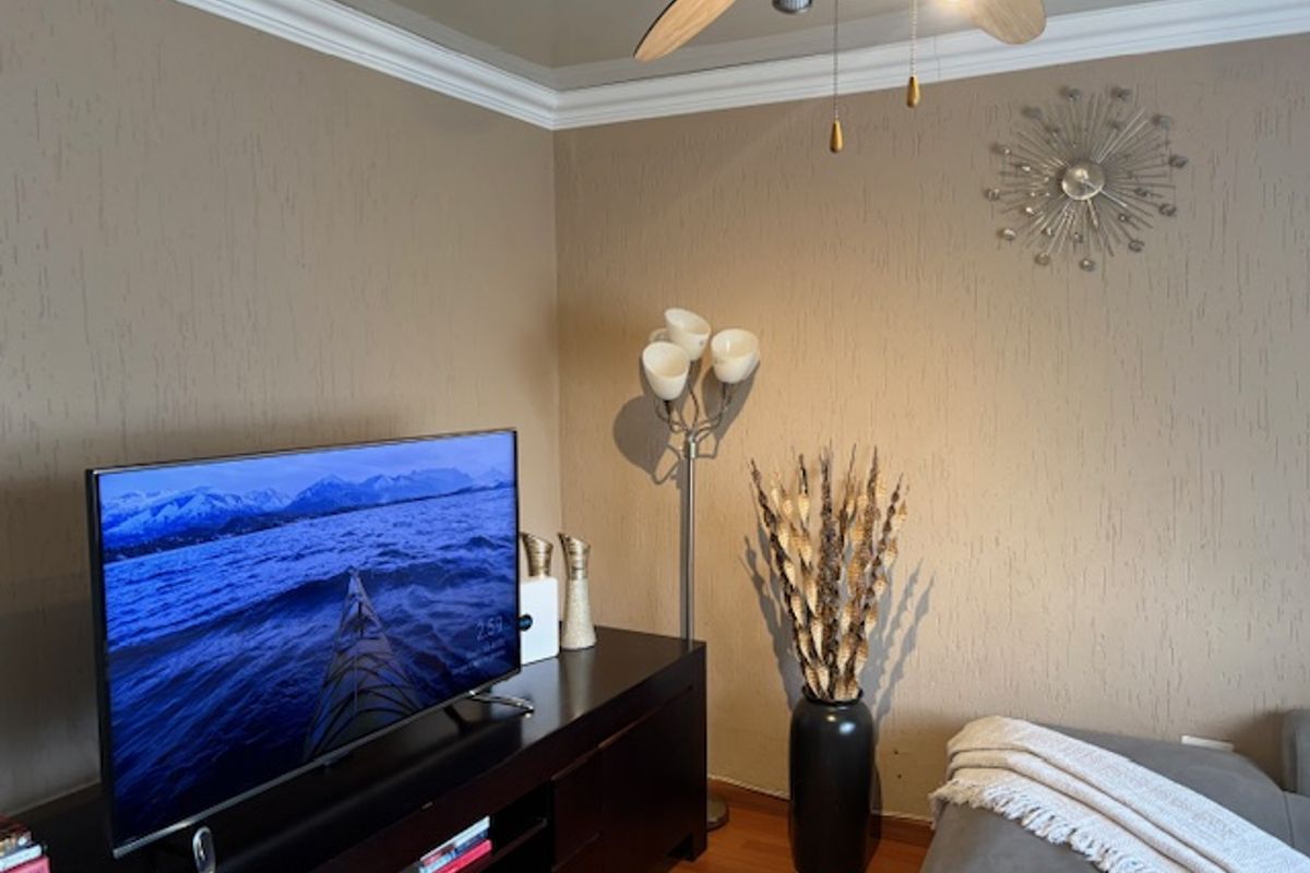 A living room area featuring hardwood flooring, decorative ceiling cornicing, and a ceiling fan, providing a comfortable space for relaxation.